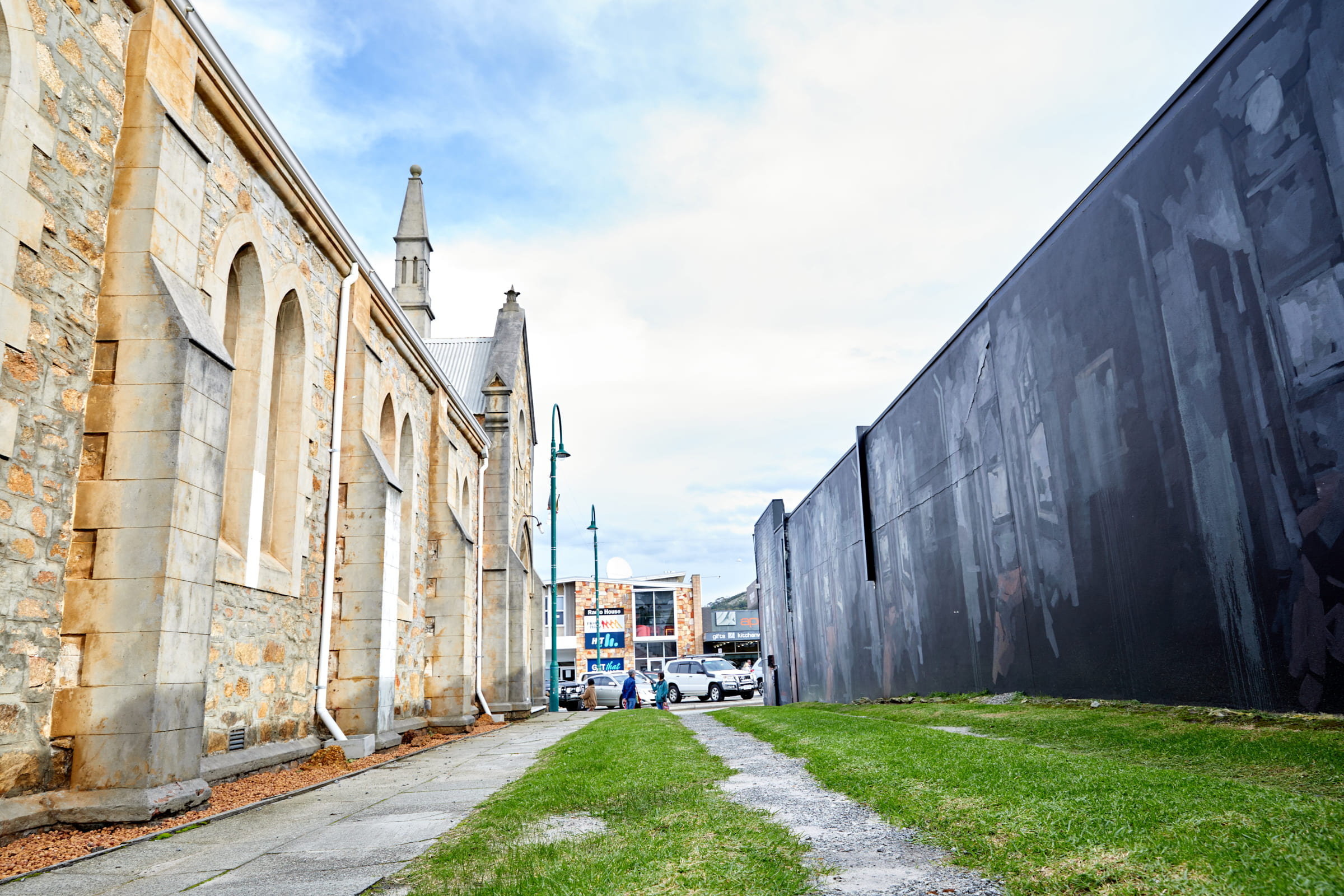 A view down a paved alleyway featuring a historic stone church on the left and a large, dark mural on the right wall, showcasing Albany Arts.