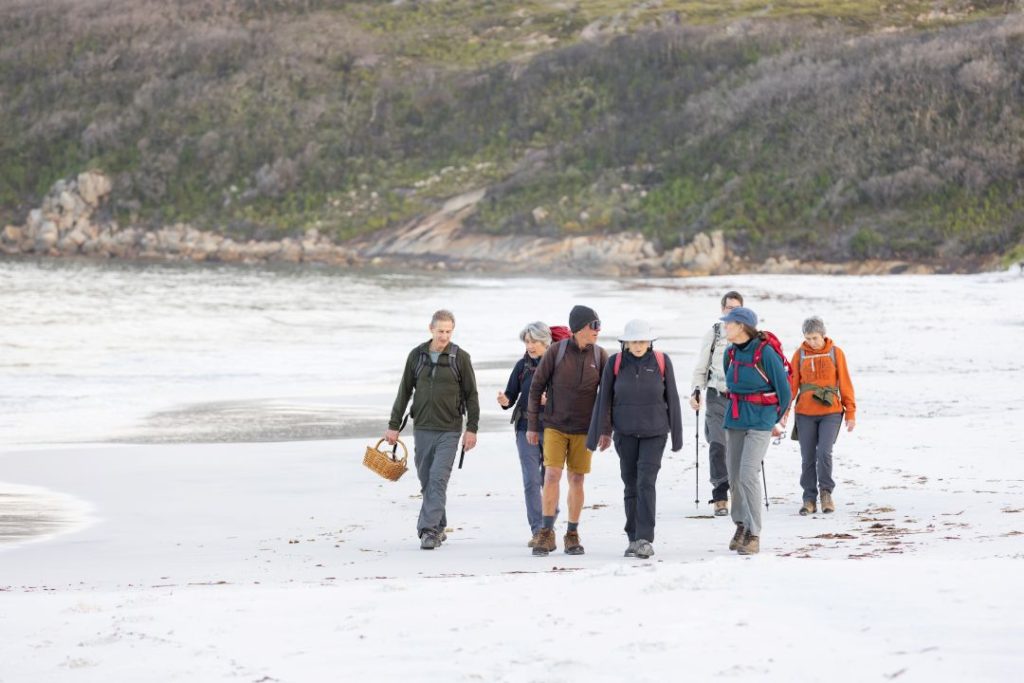 group of hikers walking along a white sandy beach towards the camera