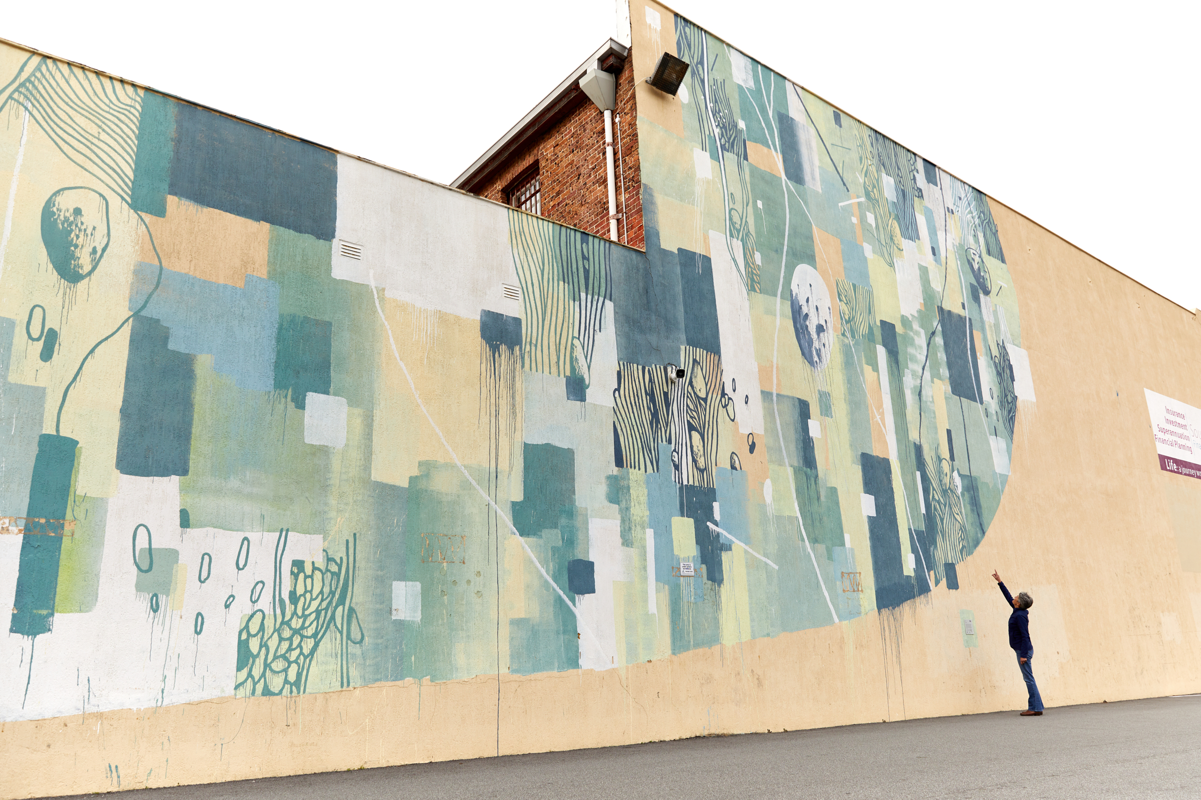 A person pointing up at a large green and blue abstract mural on the side of a building.